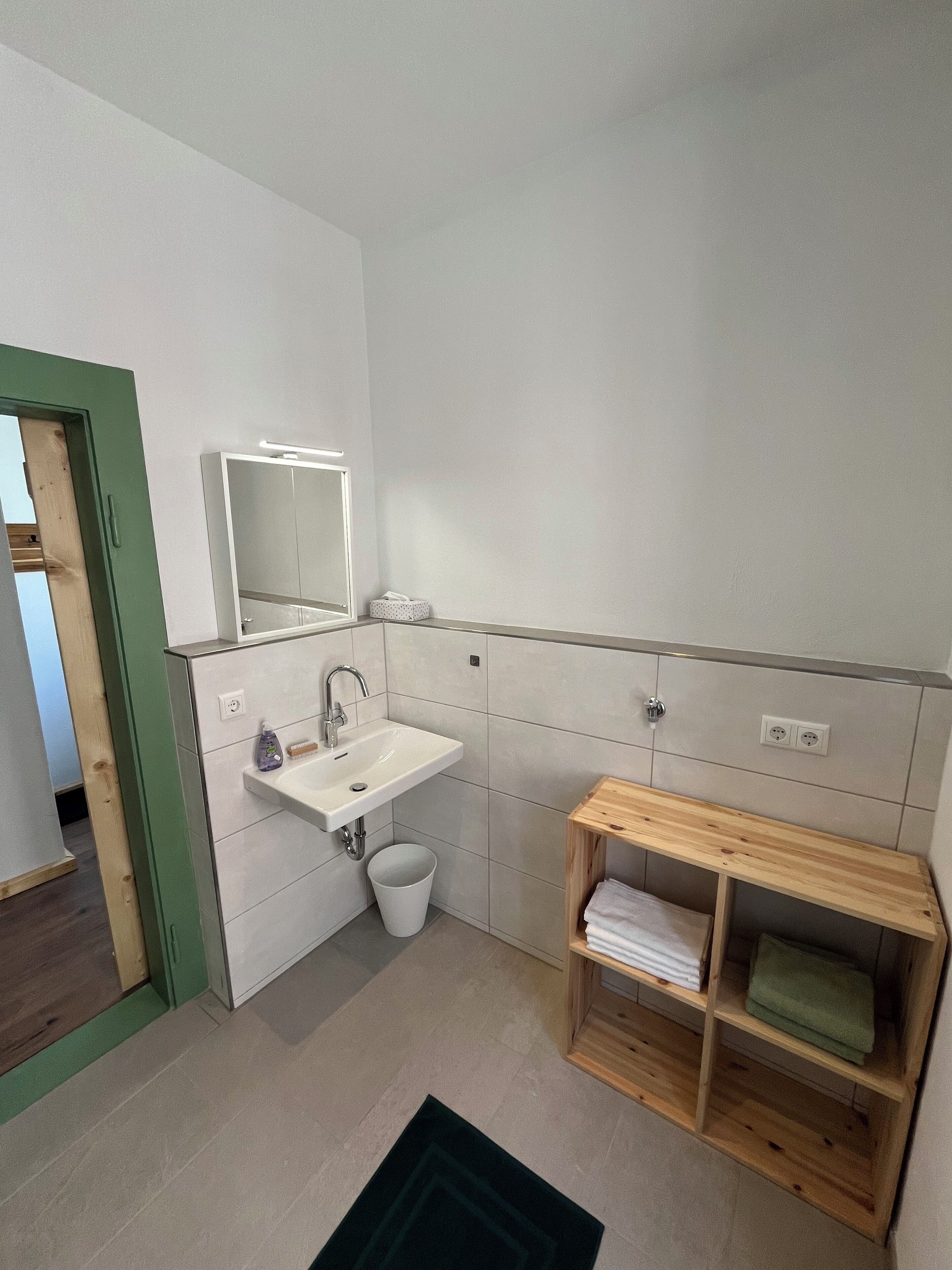 Un baño moderno con un lavabo blanco, espejo y estante de madera.