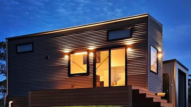 Une maison moderne à deux étages, dotée de grandes fenêtres, d’un escalier et d’une pelouse bien entretenue.