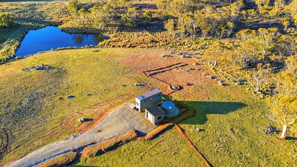 An aerial view of a rural property with a small building, a pond, and scattered trees.