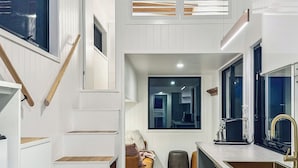 Une cuisine moderne avec des meubles blancs, un plancher en bois, un four encastré et une grande fenêtre.