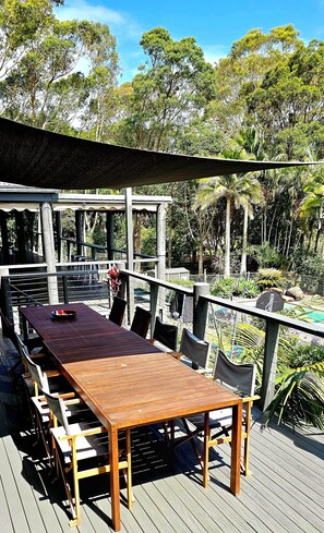 Una terrazza esterna con tavolo e sedie in legno, immersa nel verde e alberi.