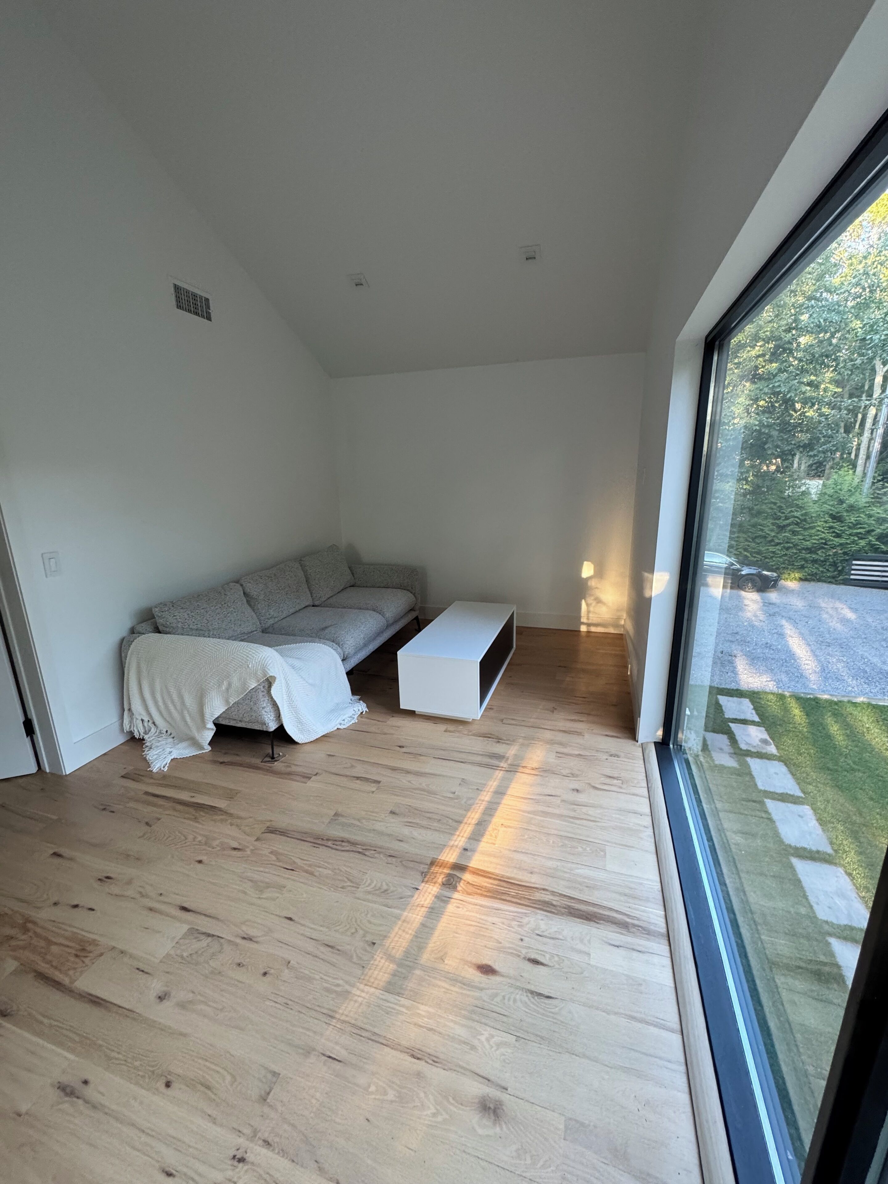 A modern living room with a sofa, a white coffee table, and a large window offering a view of a garden.