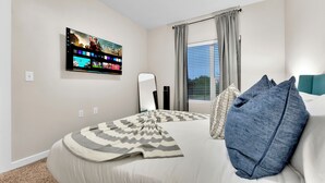 Quarto de hotel com cama, televisão na parede exibindo um filme, janela com cortinas e vista para o exterior.