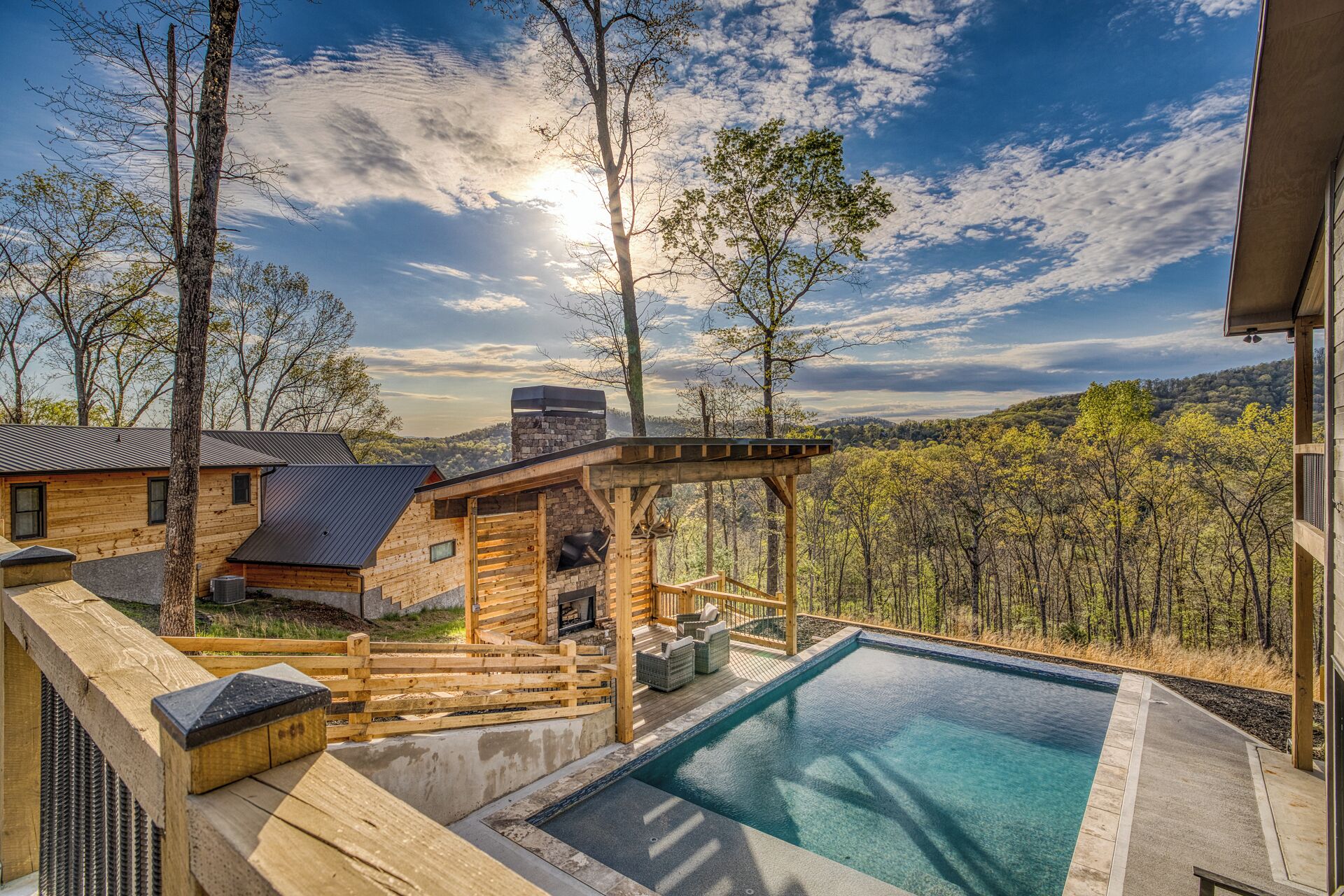 A wooden cabin with a swimming pool, surrounded by trees and a view of a forested area.