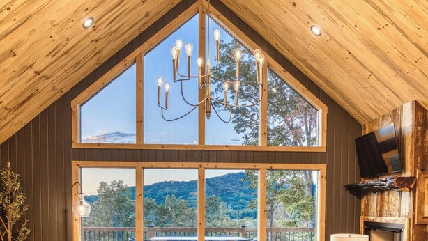 Un'ampia stanza con grandi finestre che si affacciano sulle montagne, un lampadario e una TV a schermo piatto montata a parete.