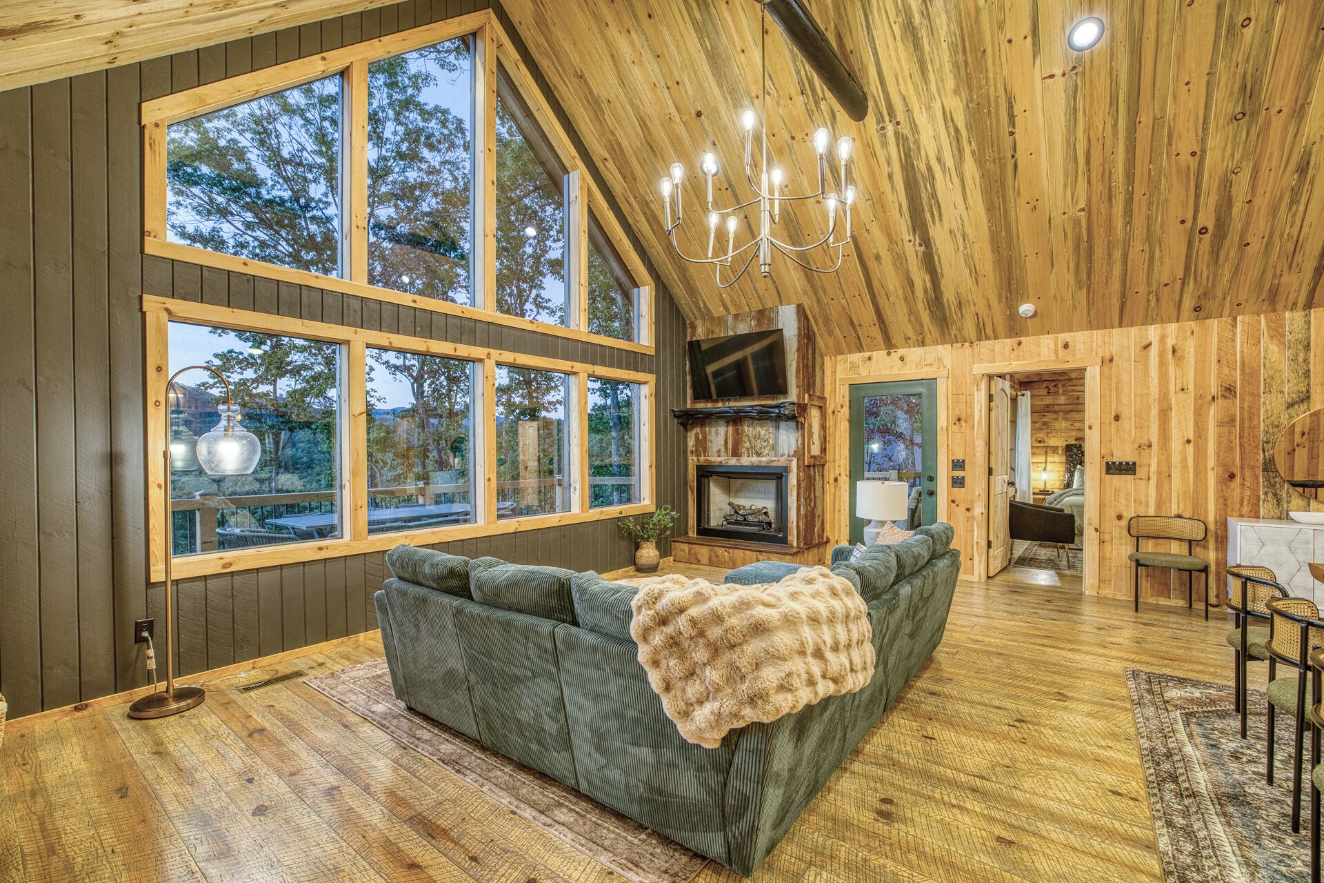 A cozy cabin interior with a large window, a fireplace, and a comfortable seating area.