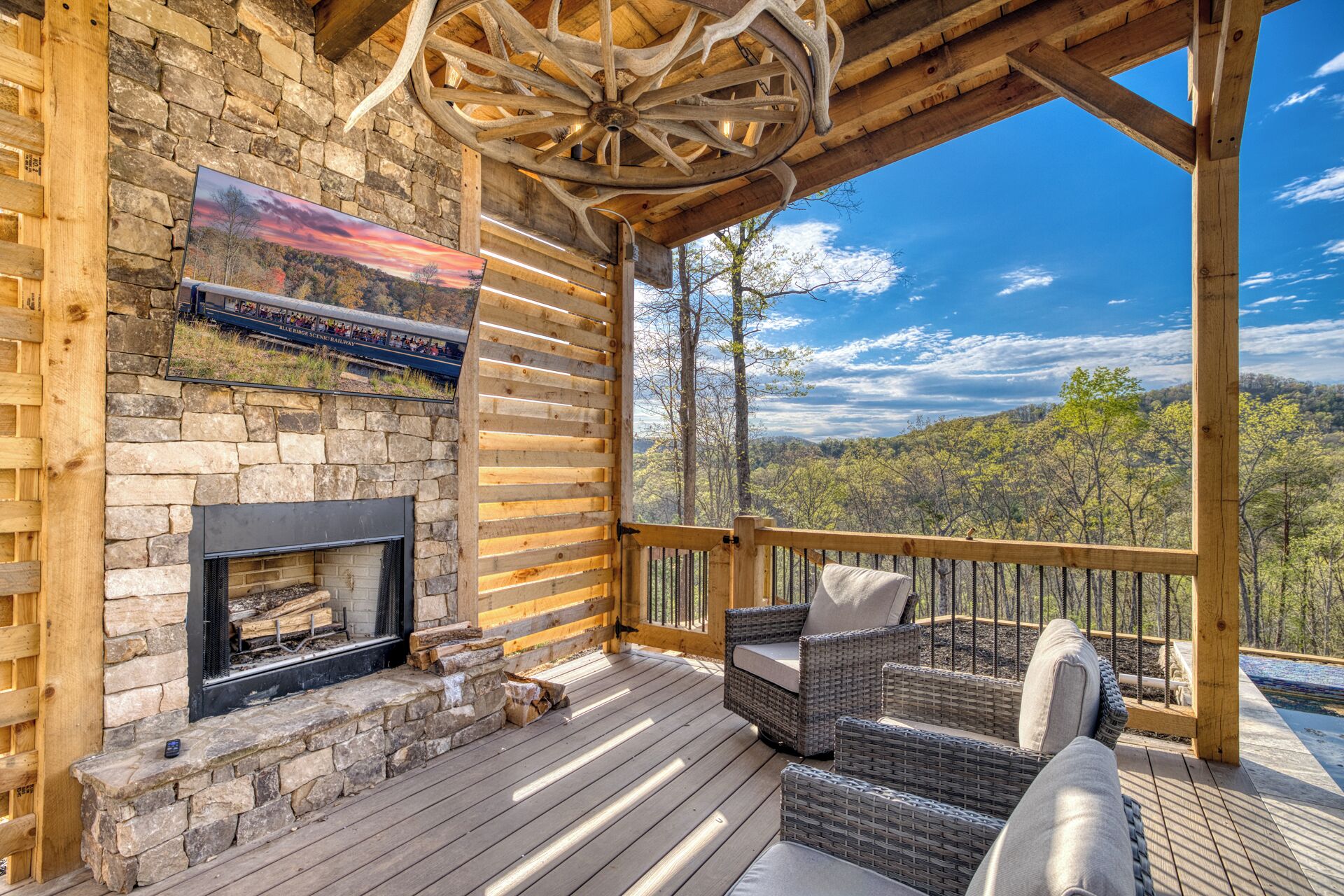 A wooden deck with a fireplace, wicker furniture, and a scenic view of a forest.