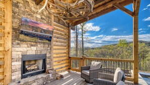 Un terrazza in legno con un camino, mobili in vimini e una vista panoramica su una foresta.