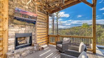 A wooden deck with a fireplace, wicker furniture, and a scenic view of a forest.