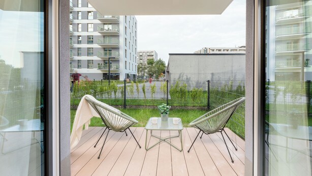 A balcony with two chairs and a small table, overlooking a fenced garden and residential buildings.