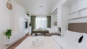 A modern hotel room with a bed, bedside tables, a TV, and a window with curtains.