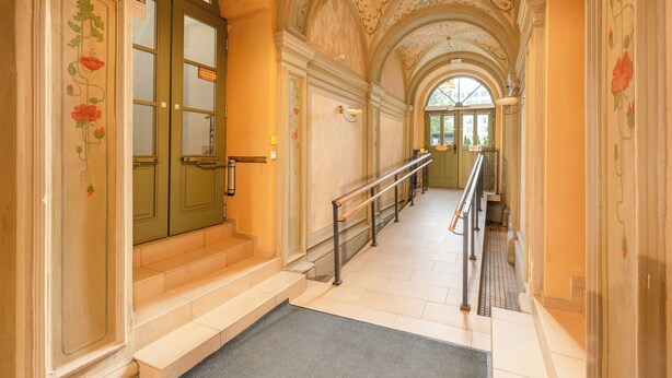 Un couloir avec des portes vertes, un escalier en marbre et un plafond décoratif.