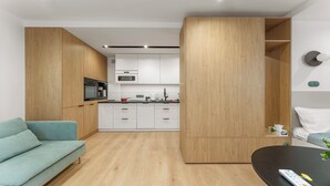 A modern kitchen with white cabinets, a black countertop, and wooden accents. There is a teal sofa and a black table with a remote control. - Kluczborska Chic Studio (Kraków)