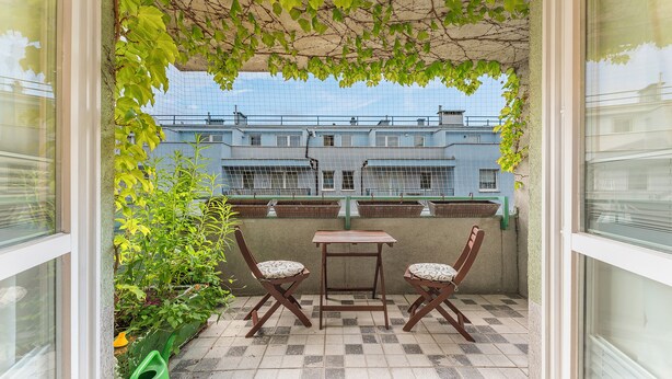 A small outdoor seating area with a table and two chairs, surrounded by greenery and overlooking a blue building. - Kluczborska Chic Studio (Kraków)