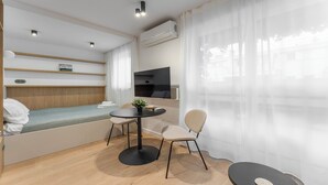 A compact, modern room with a bed, a small table, a chair, an air conditioning unit, and a TV mounted on the wall. - Kluczborska Chic Studio (Kraków)