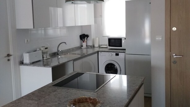 Una cocina moderna con gabinetes blancos, una campana extractora de acero inoxidable, un lavavajillas integrado y un microondas.