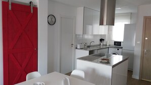 Una cocina compacta con armarios blancos, una campana extractora de acero inoxidable, un microondas y un lavamanos.