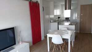 Una cocina moderna con armarios blancos, una puerta roja y un comedor con una mesa y sillas blancas.