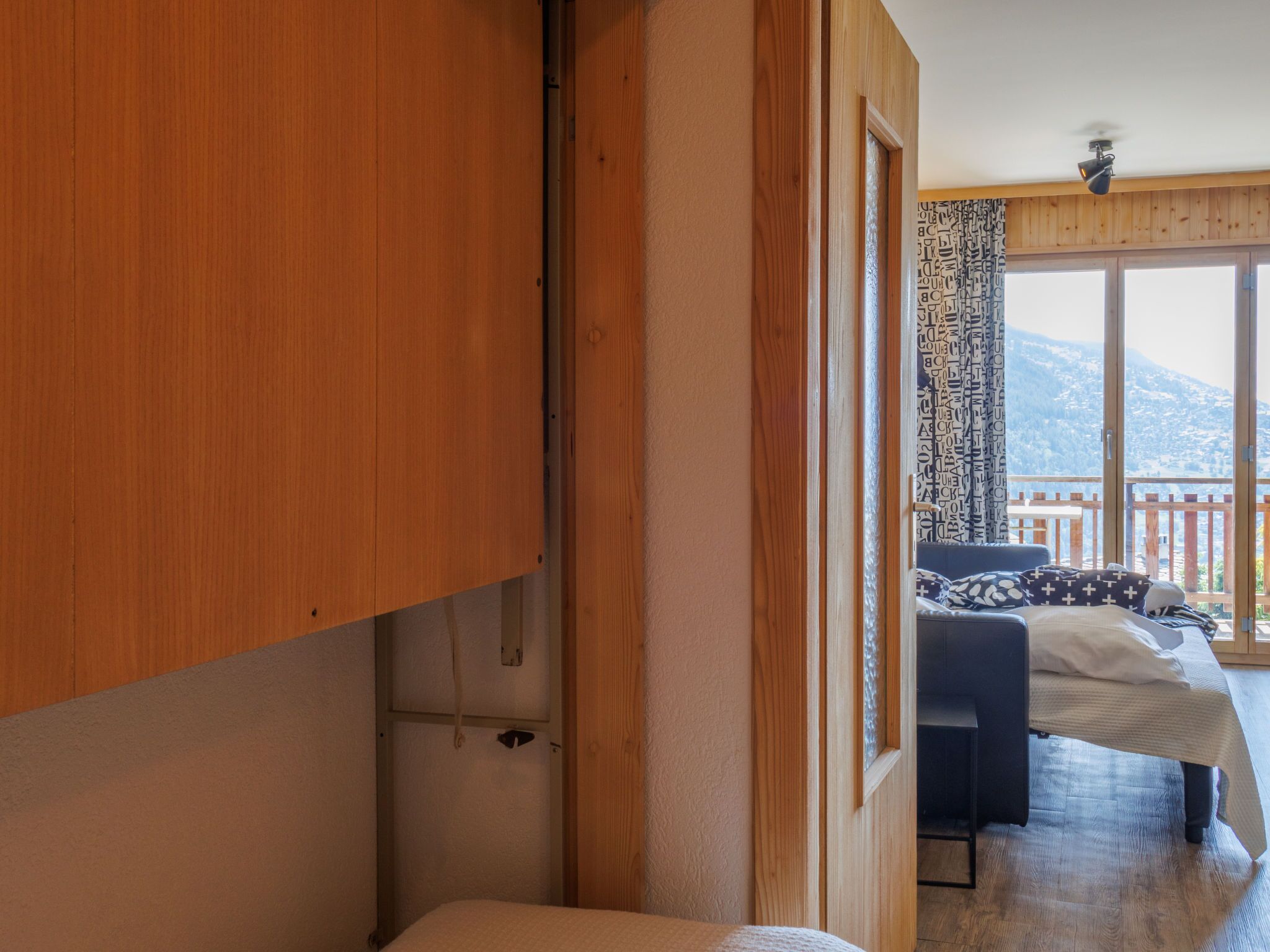 Una habitación con cama, armario de madera y balcón con vistas a las montañas.