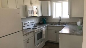 A kitchen with white cabinets, a stainless steel sink, a microwave, a stove, and a window providing natural light.