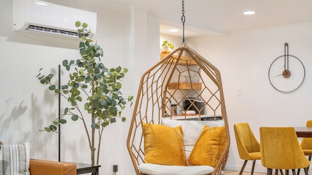 Un espace repas moderne avec un fauteuil suspendu, des chaises jaunes et une plante.