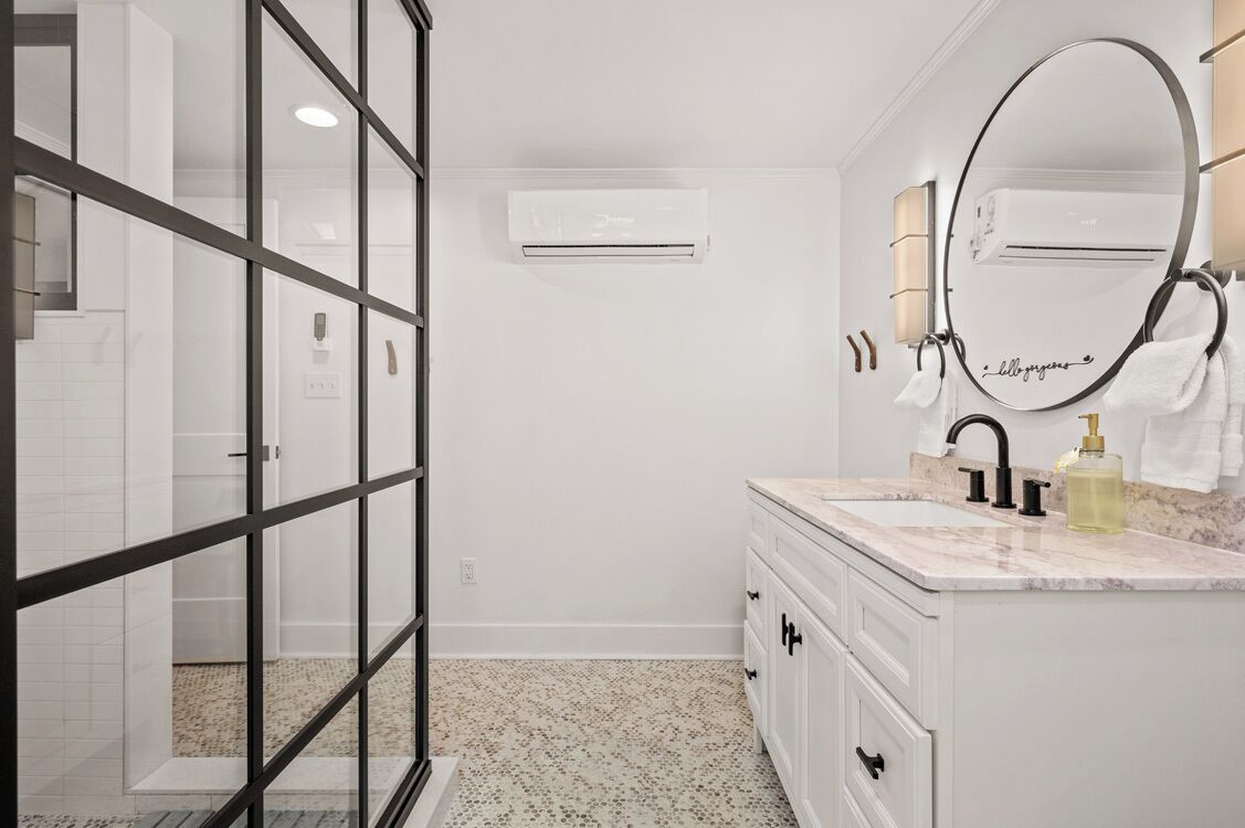 A modern bathroom with a glass shower enclosure, a white vanity with a marble countertop, and a large mirror with a towel ring.