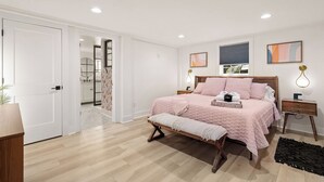 Une chambre à coucher comprenant un lit, des tables de chevet, un banc et une porte donnant sur une salle de bain.