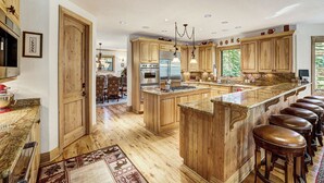 A spacious kitchen with wooden cabinets, a central island, and a bar area with stools. - NEW Cedar Lodge on Peak 8 | Private Hot Tub, Firepit, Grill & Easy Shuttle Access (Breckenridge)