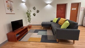 Una sala de estar con sofá, televisor, planta en maceta y obra de arte en la pared.