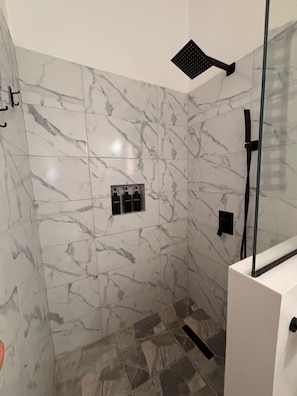 A shower area with marble walls, a glass enclosure, and a black towel rack.
