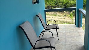 Un espacio de estar al aire libre techado con dos sillas de metal y un ventanal pequeño.