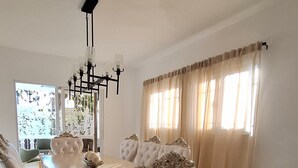 A dining area with a large table and ornate chairs, a chandelier, and a television.