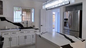 A modern kitchen with white cabinetry, a large island, and a stainless steel refrigerator.