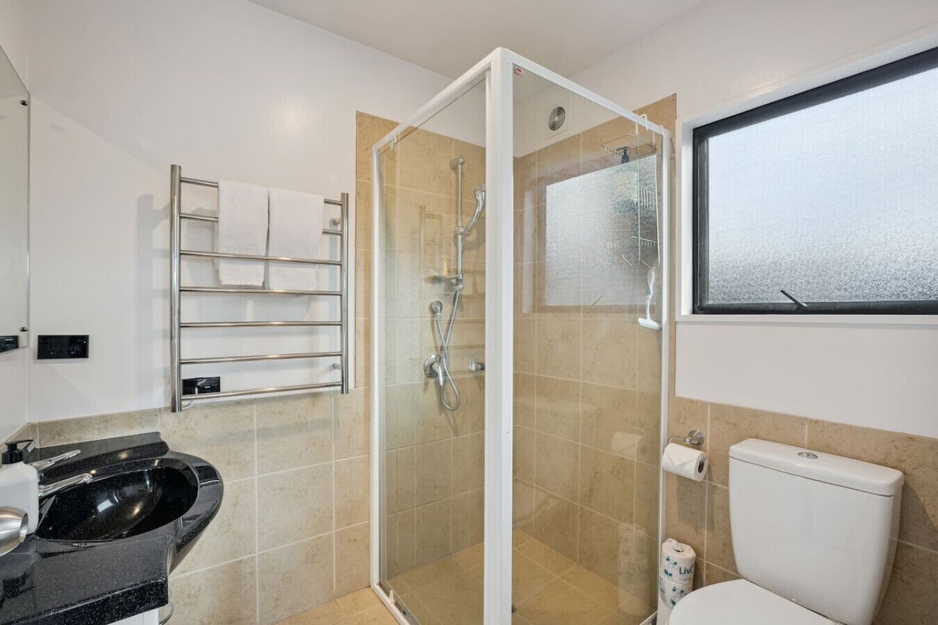 A modern bathroom with a glass-enclosed shower, a toilet, a sink, and a towel rack.