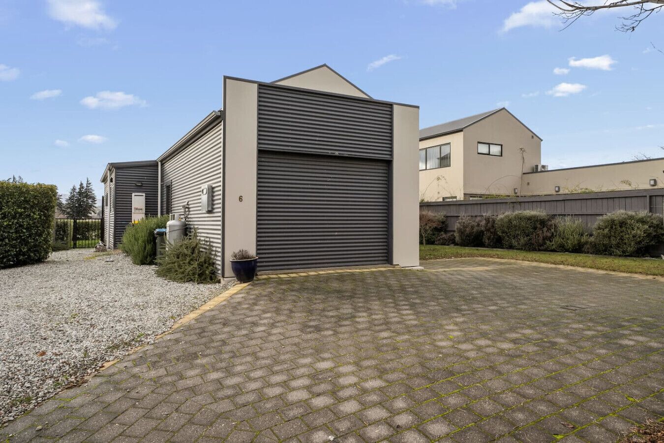 Een modern gebouw met een grote garagepoort, een grindpad en omliggend groen.