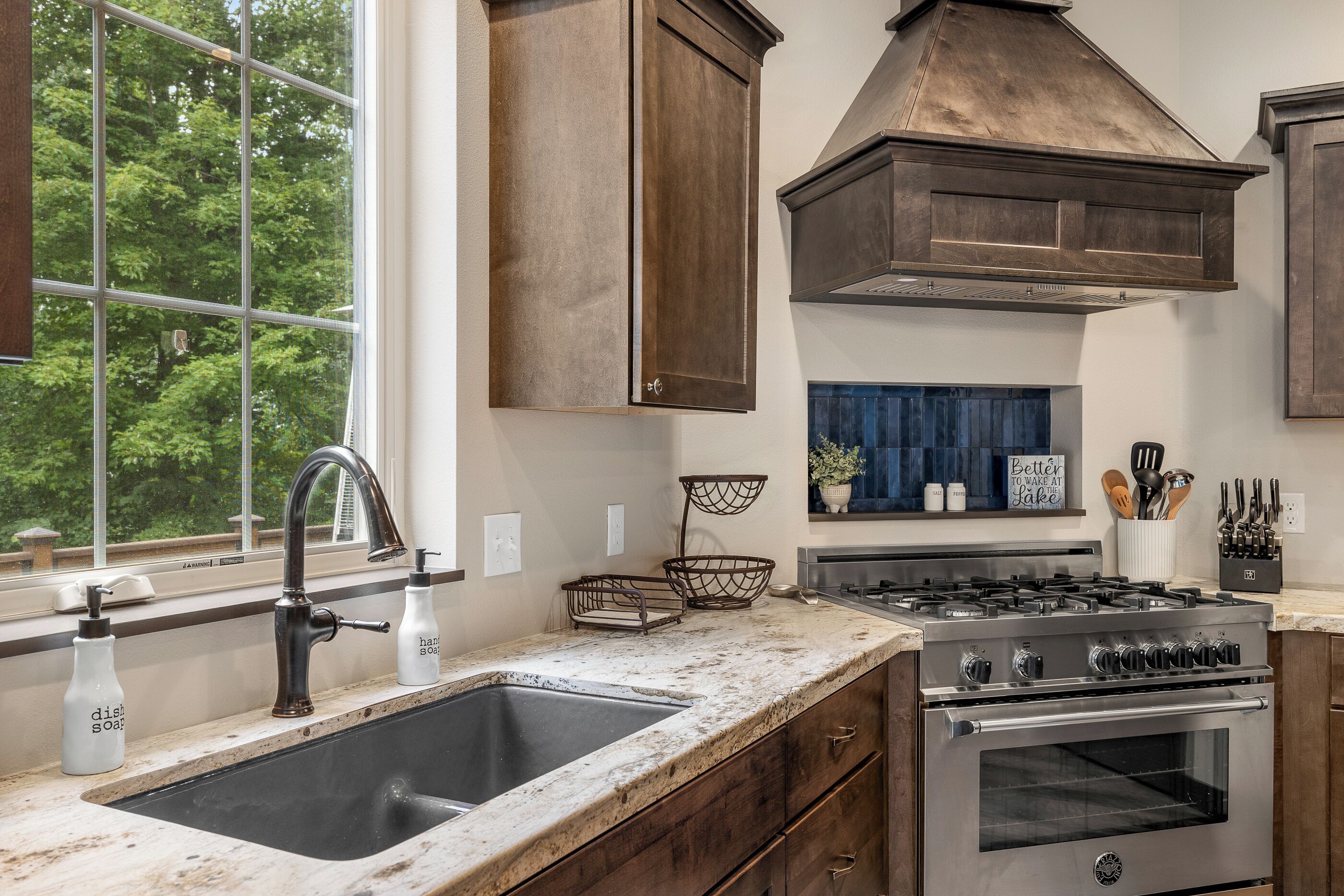A kitchen with a double sink, stainless steel stove, and wooden cabinets.