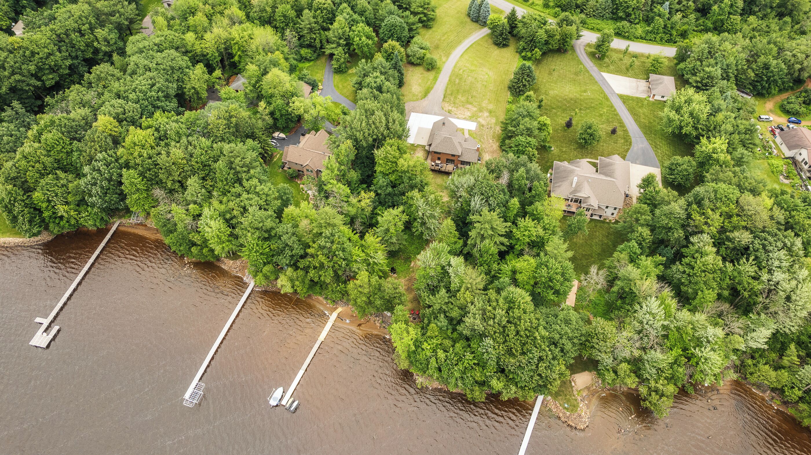 An aerial view of a residential area with houses surrounded by dense greenery and a body of water with docks.