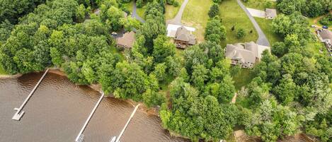 An aerial view of a residential area with houses surrounded by dense greenery and a body of water with docks.