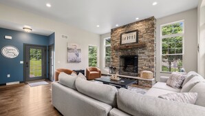 A modern living room with a stone fireplace, a large sofa, a coffee table, and a view of the outdoors through large windows.