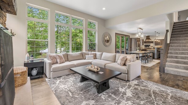 A spacious living room with a large sectional sofa, a coffee table, and a fireplace. There are large windows providing natural light and a view of the outdoors.