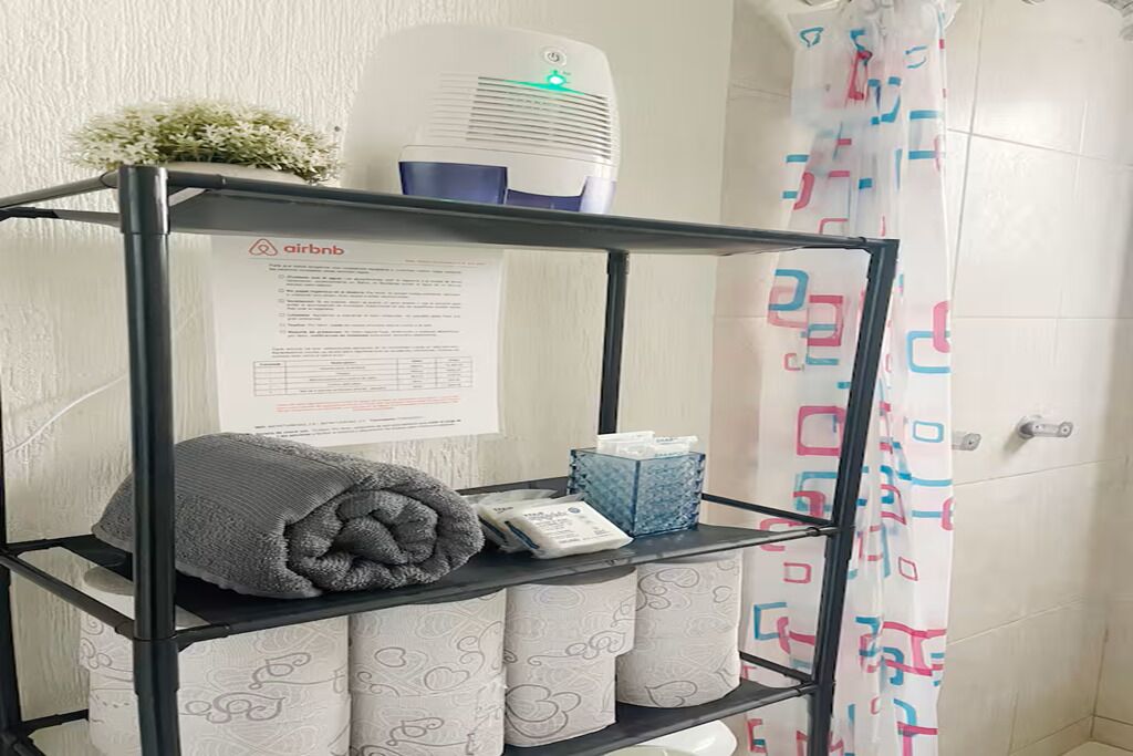 Un bany amb cortina de dutxa, un penjador de tovalloles i tovalloles, una caixa de mocadors i un paper amb el logotip d'Airbnb.
