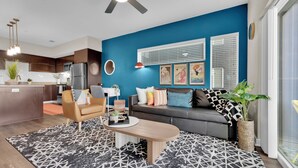 A modern living room with a blue accent wall, a sofa, a coffee table, and a kitchen area in the background. - Charming 1-bedroom apartment with AC, WiFi in delightful Cedar Park (Cedar Park)