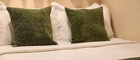 Una cama con ropa blanca y dos almohadas verdes.