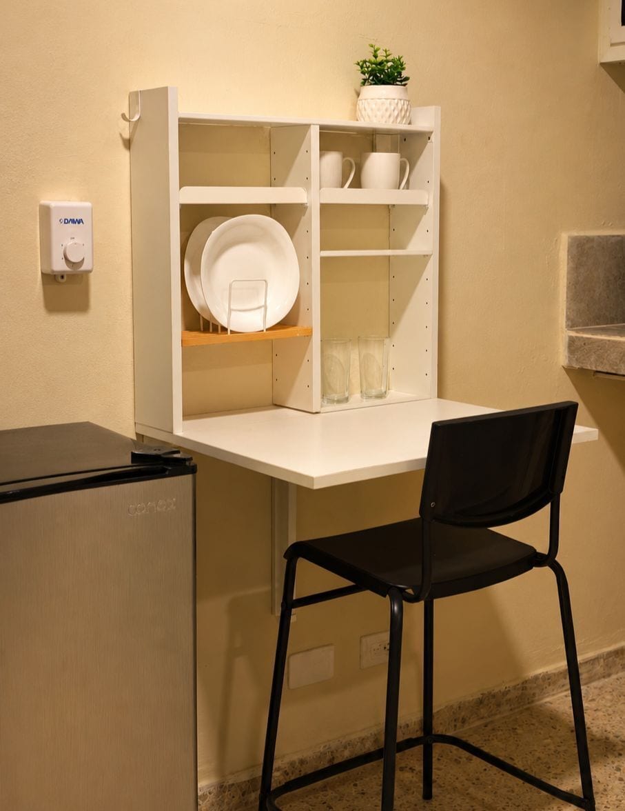 A kitchenette with a white countertop, a black chair, and a small refrigerator.