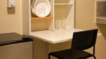 A kitchenette with a white countertop, a black chair, and a small refrigerator.