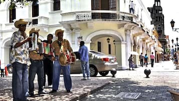 A street scene with musicians performing on a sidewalk in front of a white building with classical architecture.
