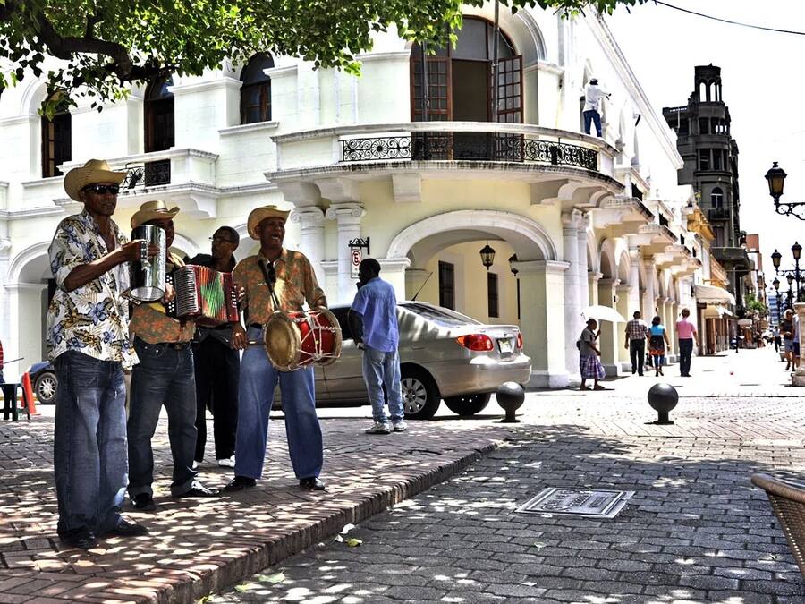 A street scene with musicians performing on a sidewalk in front of a white building with classical architecture.