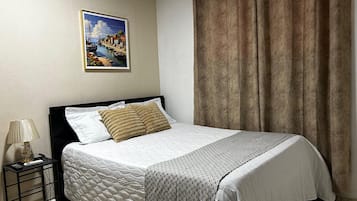 Uma cama bem arrumada com cobre acolchoado, um quadro emoldurado acima e uma cortina na janela.
