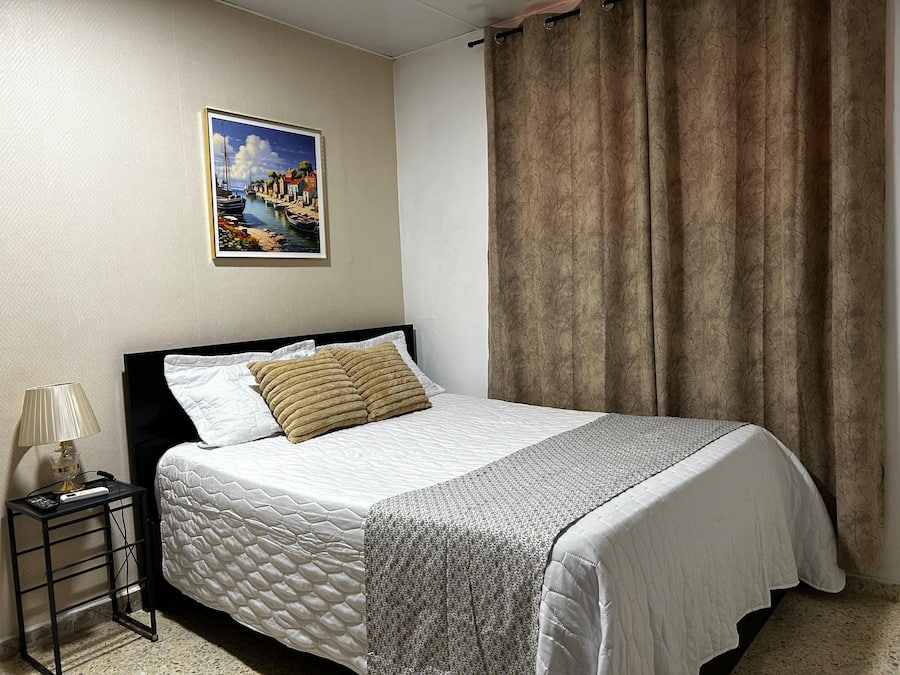 Uma cama bem arrumada com cobre acolchoado, um quadro emoldurado acima e uma cortina na janela.