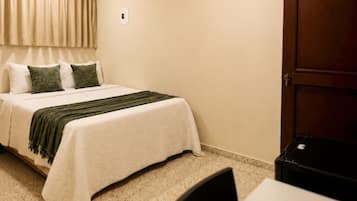 A hotel room with a bed, a desk, a chair, a ceiling fan, and a door.